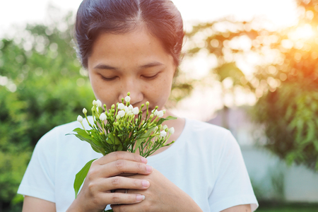 Asian woman smelling flowers in garden.の写真素材