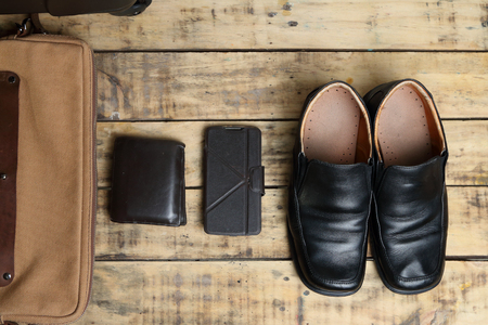 Black leather shoes, wallet, mobile smart phone and  luggage travel bag on the wooden tableの写真素材