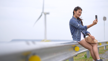 Asian women are photographing selfie from a mobile phone, with the background being a wind turbine and a meadow.の写真素材
