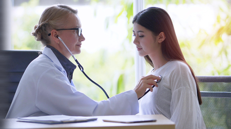 Senior female doctor checking examining a woman by stethoscope in office hospital.の写真素材