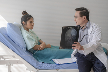The senior male doctor talked about the patient's illness by explaining the X-ray film in the patient's bed.の写真素材