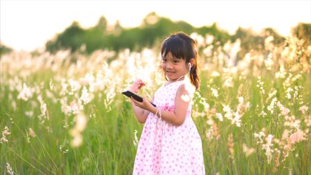 Asian girl listen to music and sing happily at the grass fields.の写真素材