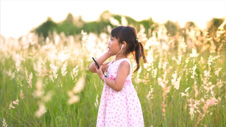 Asian girl listen to music and sing happily at the grass fields.の写真素材