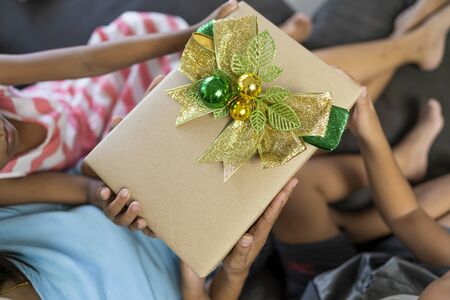 The hand of a woman, a girl and a boy with a brown christmas gift boxの写真素材