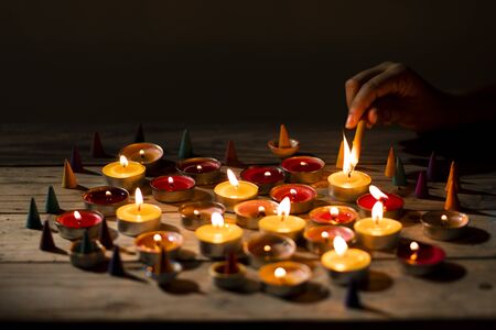 Hand lit lighting candle on wood table. Many candle flames in darkness.の写真素材