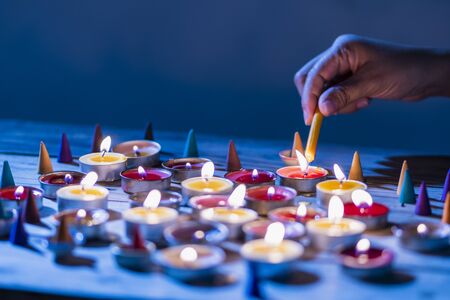 Hand lit lighting candle on wood table. Many candle flames in darkness.の写真素材