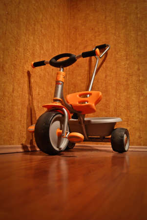 Orange tricycle in the corner of the roomの写真素材