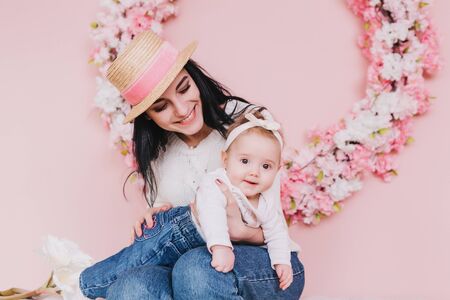Mother and child girl playing, kissing and hugging on pink background with flowers.の写真素材