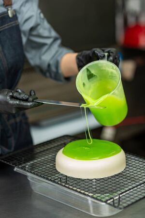 Hands of a confectioner in gloves make a cake in green glazeの写真素材