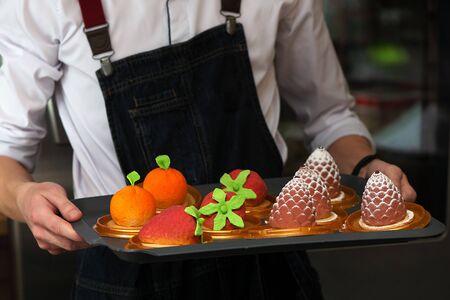 The waiter advertises cakes in the form of fruits, berries and cones on a trayの写真素材
