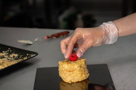 Confectioner in gloves makes a cake with cream and raspberries, sprinkled with crumbs