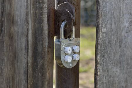 Old padlock code lock hanging on a wooden gateの写真素材