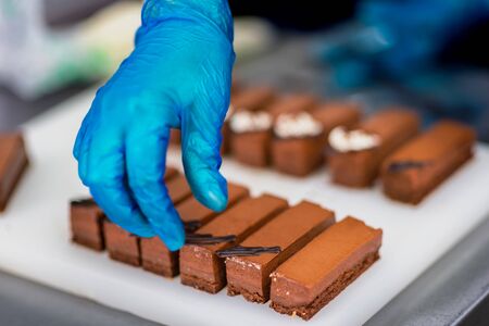Hands of a confectioner with gloves make a chocolate cakeの写真素材