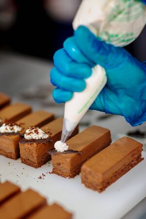 Hands of a confectioner with gloves make a chocolate cakeの写真素材