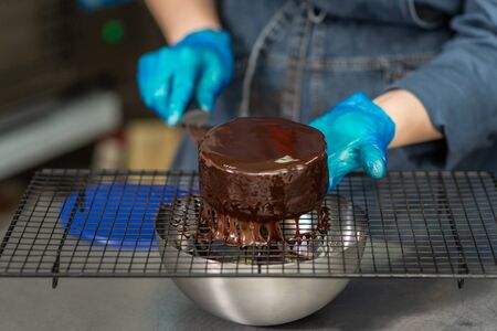 Hands of a confectioner with gloves make a chocolate cakeの写真素材