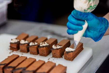 Hands of a confectioner with gloves make a chocolate cakeの写真素材