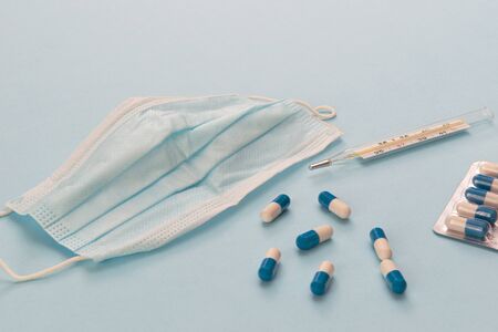 White and blue pills, glass mercury thermometer, face mask on a blue background