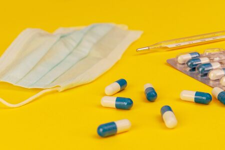 White and blue pills, glass mercury thermometer, face mask on a blue background