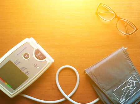 Digital blood pressure gauge and glasses are on the brown backgroundの写真素材
