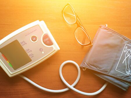 Digital blood pressure gauge and glasses are on the brown background. Illustration on theme of life and health care of senior adults, hypertonia - poor eyesight. sunlight tone.の写真素材