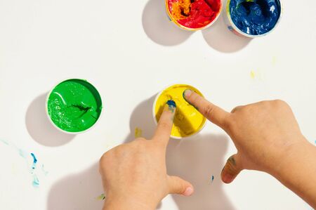 Two childrens fingers are over tube of yellow dyeの写真素材