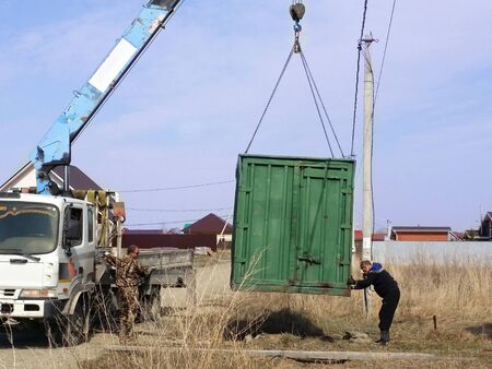 Green cargo container which gray boom with blue hook of truck manipulator put on the ground near the power line.のeditorial素材