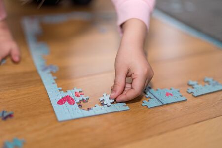 Blond girl in a pink sweater playing with a jigsaw on the floor by the confinement of coronavirus covid-19の写真素材