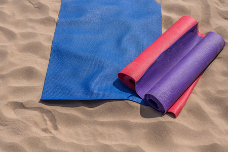 Three colorful yoga mats lie on the sand under the sun waiting for the lesson: a variety of outdoor activities while on vacationの写真素材
