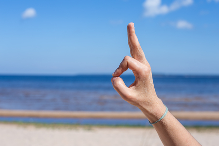 Female hand: fingers in the form of yogic gesture against the blue sea and sky.の写真素材