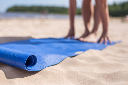 Blue mat and blurred in the background hands and feet. Girl doing yoga on a sunny day at the beach.の写真素材
