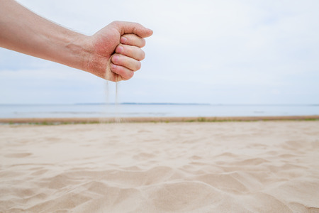 The sand runs through clenched fist. On the background - calm seaの写真素材