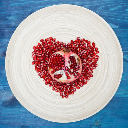 peeled pomegranate seeds on a plate in the form of heartの写真素材