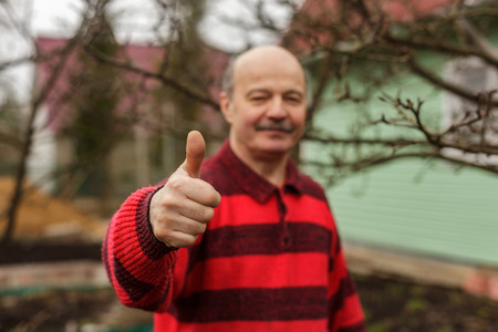 Elderly man with a mustache and a sweater showing thumb as an endorsementの写真素材