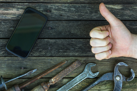 Repair phone using tools. Old workshop with new technologies. The background for the carpentry work. Approval of work with thumb upの写真素材