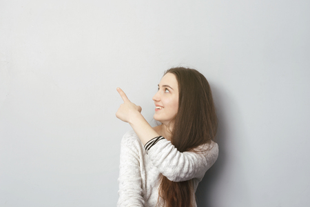Girl with long hair shows index finger up, attracting attentionの写真素材