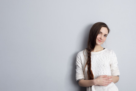 Beautiful girl with a plait hairstyle standing at the gray wall and cute smilesの写真素材