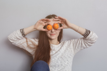 Girl with long hair fooling around, closing her eyes with tangerinesの写真素材