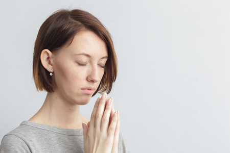 Girl holding hands together, elbows to the sides. Eyes closed. Meditate or make a wish, trying to...