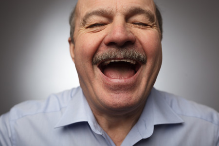 Elderly man laughs from ear to ear, giggles on the funny stories. Eyes closed. Be happy of news or eventsの写真素材
