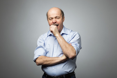 Bald man covers mouth with fist, yawning with fatigue and sleepiness. Tired of the work and desire to sleepの写真素材