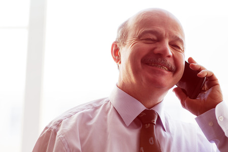 elderly man in a tie carefully listen to the interlocutor on the phone. happy looking away.の写真素材
