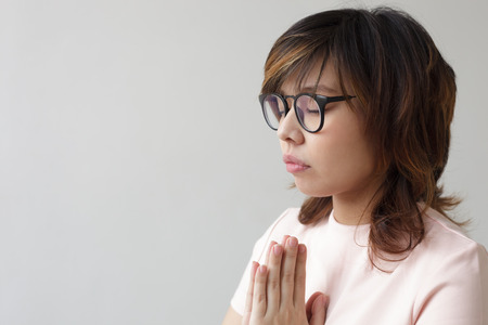 Asian girl in glasses with closed eyes think about future, praying to Godの写真素材