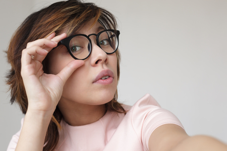 Japanese girl corrects glasses. She looks into the camera doubtfullyの写真素材