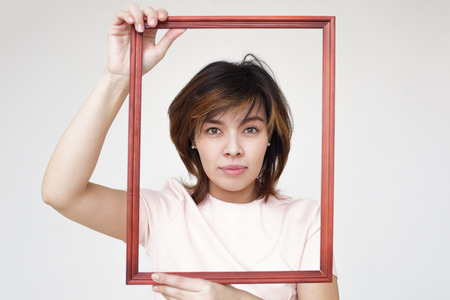 Confident beautiful girl holding a picture frame and smiling. The picture for the family album of memoriesの写真素材