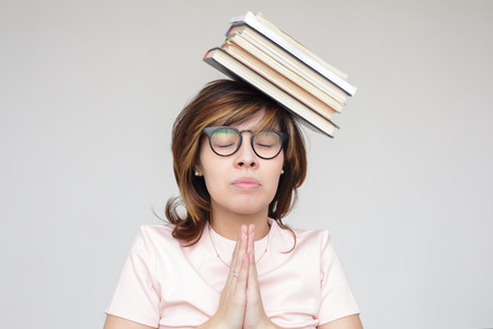 Girl meditates with a pile of books on head. Preparing for the exam, or reading booksの写真素材