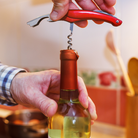 A man opens a bottle of white wine with a corkscrewの写真素材