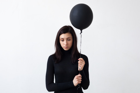 A sad girl holds a black balloon in her hands. She is sad for the loneliness and devastation of the soulの写真素材