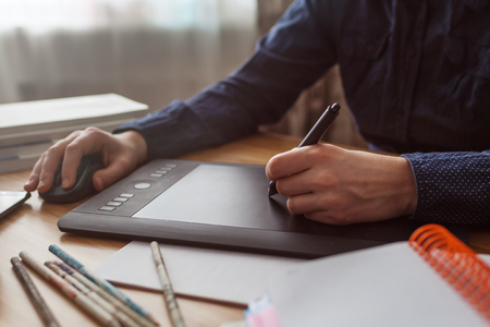 Workplace of designer. Graphic tablet surrounded by phone, camera, pencils and books. Illustrator draws a sketchの写真素材