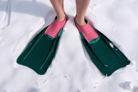 An athlete in swimming fins stands on the snow. To mix up the time or the cold weather in summerの写真素材