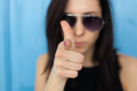 Blurred portrait of a girl in sunglasses. She points to the index finger, pointing to the viewer.の写真素材